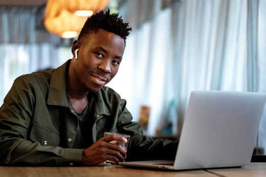Cheerful african american man in headphones using computer in cafe. young smiling businessman working on laptop. copy space
