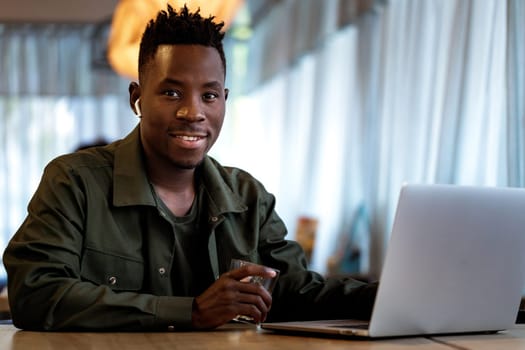 Cheerful african american man in headphones using computer in cafe. young smiling businessman working on laptop. space for text. man looking at the camera