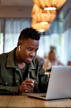 Cheerful young african american man in headphones using computer in cafe