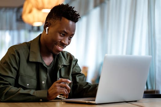 Cheerful african american man in headphones using computer in cafe. young smiling businessman working on laptop. copy space