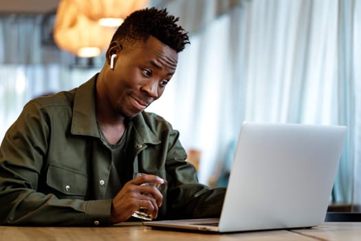 Cheerful african american man in headphones using computer in cafe. young smiling businessman working on laptop. space for text