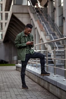 young african american man in jacket messaging online, checking social networks outdoor