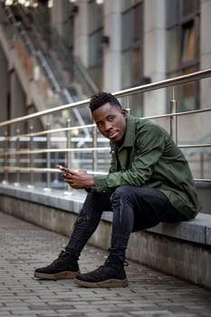 young african american man in jacket messaging online, checking social networks outdoor