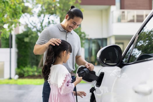 Progressive father and daughter returned from school in electric vehicle that is being charged at home. Electric vehicle driven by renewable clean energy. Home charging station concept for environment