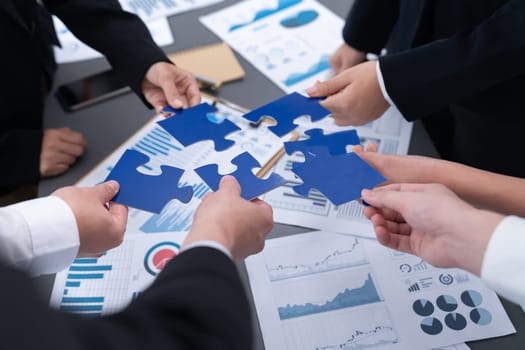 Closeup top view business team of office worker putting jigsaw puzzle together over table filled with financial report paper in workplace with manager to promote harmony concept in meeting room.