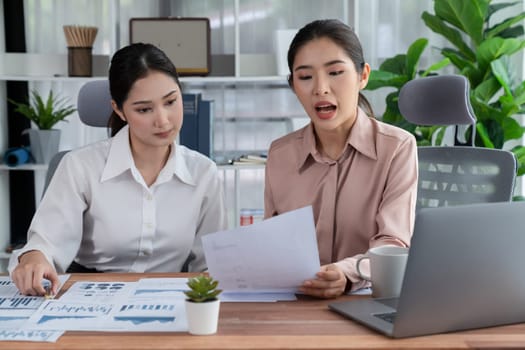 Two young office lady colleagues collaborating in modern office workspace, engaging in discussion and working together on laptop, showcasing their professionalism as modern office worker. Enthusiastic