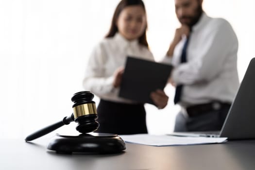 Focus closeup wooden gavel on blur background of lawyer colleagues or drafting legal documents on their workplace at law firm office. Hammer of justice for righteous and equality judgment. Equilibrium