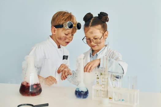 Girl with boy working together. Children in white coats plays a scientists in lab by using equipment.