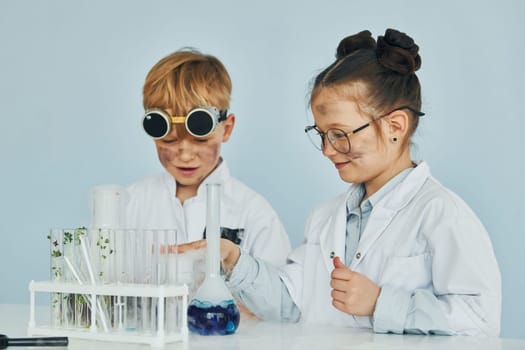 Girl with boy working together. Children in white coats plays a scientists in lab by using equipment.