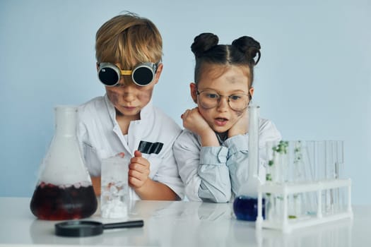 Girl with boy working together. Children in white coats plays a scientists in lab by using equipment.