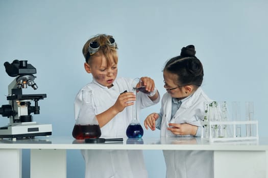 Little girl and boy in white coats plays a scientists in lab by using equipment.