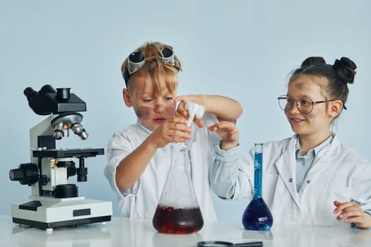 Little girl and boy in white coats plays a scientists in lab by using equipment.