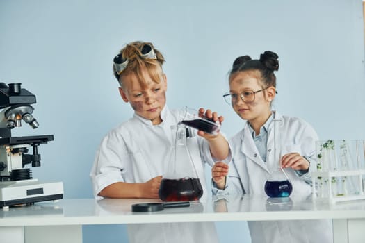 Little girl and boy in white coats plays a scientists in lab by using equipment.