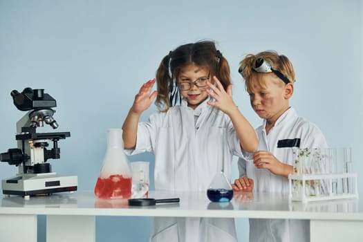 Little girl and boy in white coats plays a scientists in lab by using equipment.