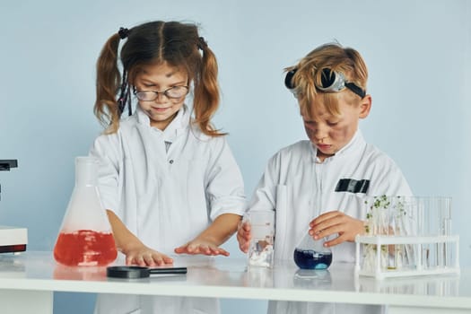 Little girl and boy in white coats plays a scientists in lab by using equipment.