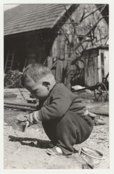 THE CZECHOSLOVAK SOCIALIST REPUBLIC - CIRCA 1970s: Vintage photo shows a small boy plays in the backyard. Retro black and white photography. Circa 1970s.
