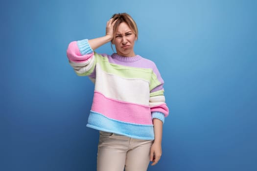 distressed blond woman in casual look holding her head on blue background.