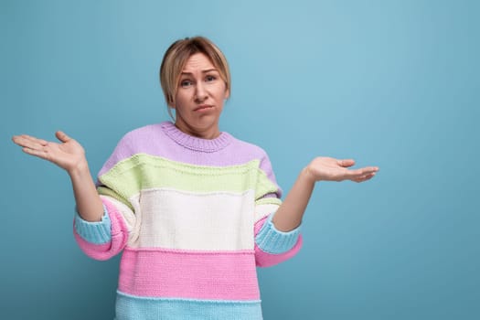doubtful blond woman in a casual look throws up her hands on a blue background.