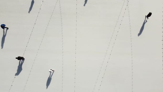 People ride on white ice rink on street and cast long shadows. People skating on sunny winter day. Top view. Aerial drone view. Leisure entertainment vacation weekend holidays activities lifestyle.