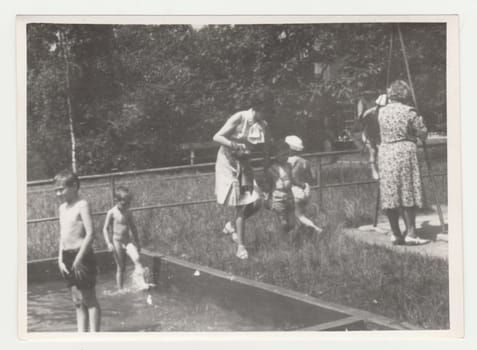 THE CZECHOSLOVAK SOCIALIST REPUBLIC - CIRCA 1970s: Vintage photo shows mothers with children at the playground - outdoor wadding pool. Retro black and white photography. Circa 1970s.