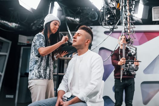 Young man is preparing for TV online broadcast. Woman helps with make up.