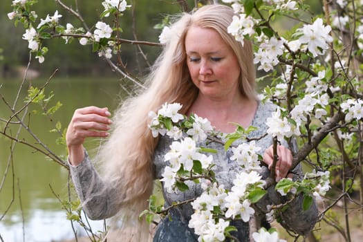 middel aged woman stands in the park next to a flowering tree, Spring time, Adult with blond hair, Wellness concept. High quality photo