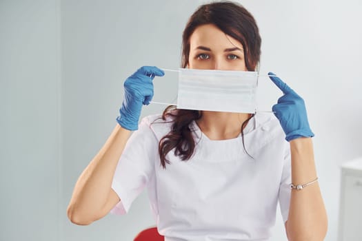 Medical mask. Portrait of professional female dentist with equipment that standing indoors.