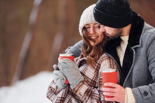 With drink. Cheerful couple have a walk in the winter forest at daytime.