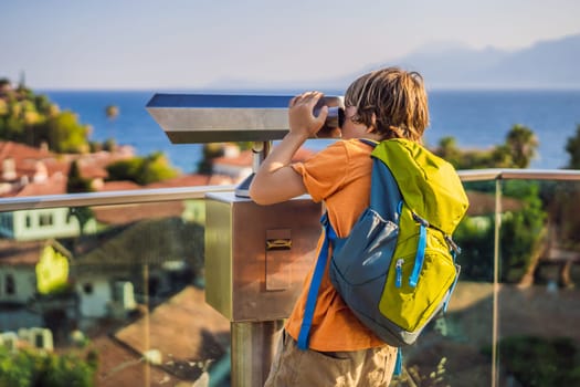 Boy tourist looks through binoculars in Old town Kaleici in Antalya. Turkiye. Panoramic view of Antalya Old Town port, Taurus mountains and Mediterrranean Sea, Turkey. Traveling with kids concept.