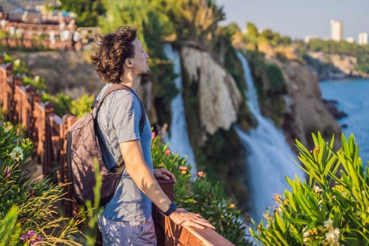 Man tourist on the background of Duden waterfall in Antalya. Famous places of Turkey. Lower Duden Falls drop off a rocky cliff falling from about 40 m into the Mediterranean Sea in amazing water clouds. Tourism and travel destination photo in Antalya, Turkey. Turkiye.
