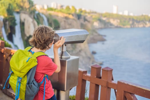 Boy tourist with a backpack on the background of Duden waterfall in Antalya. Famous places of Turkey. Lower Duden Falls drop off a rocky cliff falling from about 40 m into the Mediterranean Sea in amazing water clouds. Tourism and travel destination photo in Antalya, Turkey. Turkiye.