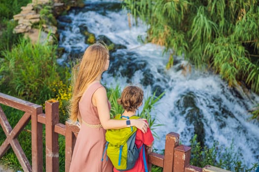 Mother and son tourists on the background of Duden waterfall in Antalya. Famous places of Turkey. Lower Duden Falls drop off a rocky cliff falling from about 40 m into the Mediterranean Sea in amazing water clouds. Tourism and travel destination photo in Antalya, Turkey. Turkiye.
