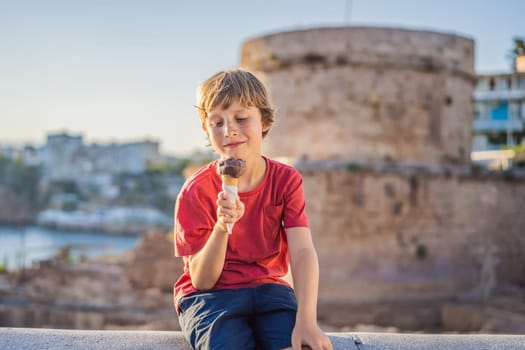 Boy tourist eating turkish ice cream on background of Hidirlik Tower in Antalya against the backdrop of the Mediterranean bay of the ancient Kaleici district, Turkey. Turkiye.