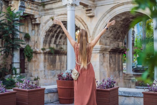 Happy female tourist traveler discover interesting places and popular attractions and walks in the old city of Antalya. Hadrian Kapisi turkey landmark city history. Popular tourist attraction - ancient Roman Hadrian Gate in old town Antalya, Turkey on a summer day. Turkiye.