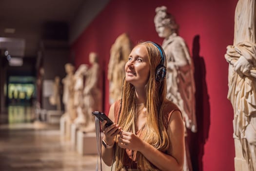 Portrait of contemporary young woman looking at sculptures and listening to audio guide at museum exhibition.