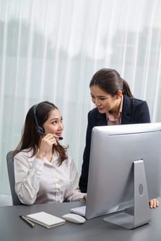 Asian female customer support operator wearing headset is guided by her supportive manager. Experienced colleague help operator handle a call with a client, providing advice and guidance. Enthusiastic