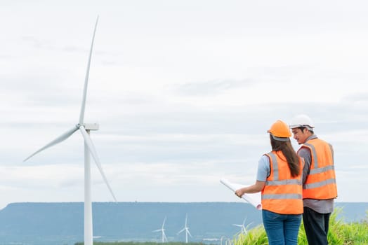 Male and female engineers working on a wind farm atop a hill or mountain in the rural. Progressive ideal for the future production of renewable, sustainable energy.