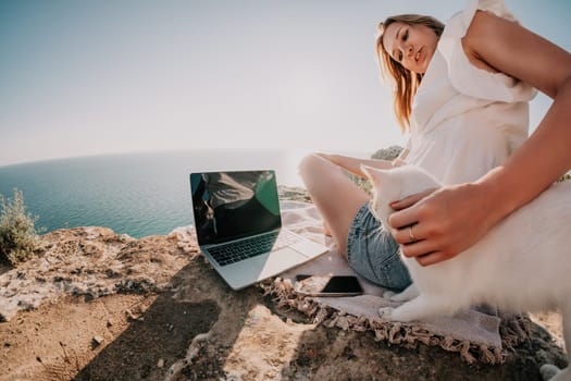 Woman sea laptop. Business woman in yellow hat working on laptop by sea. Close up on hands of pretty lady typing on computer outdoors summer day. Freelance, digital nomad, travel and holidays concept.