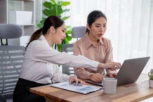 Two young office lady colleagues collaborating in modern office workspace, engaging in discussion and working together on laptop, showcasing their professionalism as modern office worker. Enthusiastic