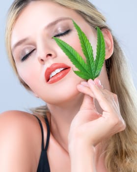 Closeup alluring beautiful woman portrait with perfect makeup lip stick, eyeshadow hold green leaf as concept for cannabis skincare cosmetic product for skin freshness treatment in isolated background