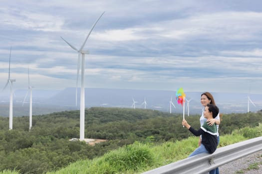 A progressive mother and her son are on vacation, enjoying the natural beauty of a lake at the bottom of a hill while the boy carries a toy windmill.