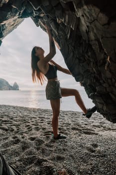 A girl climbs a rock. The athlete trains in nature. Woman overcomes difficult climbing route. Extreme hobby. Tourist woman rock climber hiking on mountains rocks over beautiful sea coast