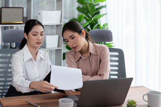 Two young office lady colleagues collaborating in modern office workspace, engaging in discussion and working together on laptop, showcasing their professionalism as modern office worker. Enthusiastic