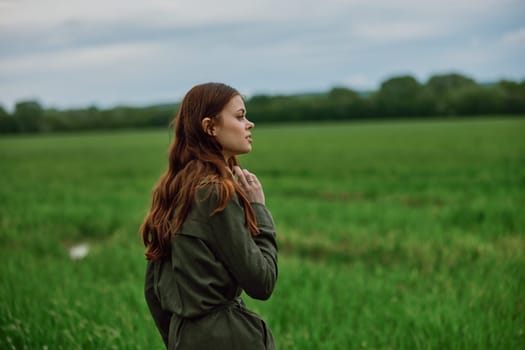 a beautiful, red-haired girl in a raincoat stands in a field in the spring in rainy weather. High quality photo