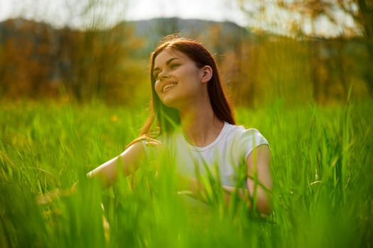 portrait of a happy woman in a white t-shirt shot through grass leaves in a field. High quality photo