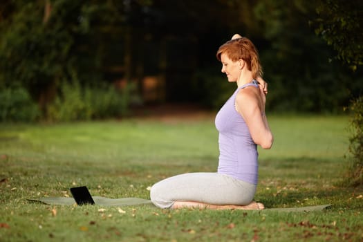 Getting some online yoga tips. an attractive woman doing yoga at the park with her tablet beside her