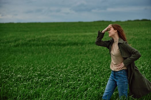 red-haired, happy woman stands in a green field in rainy weather. Emotions, harmony with nature. High quality photo