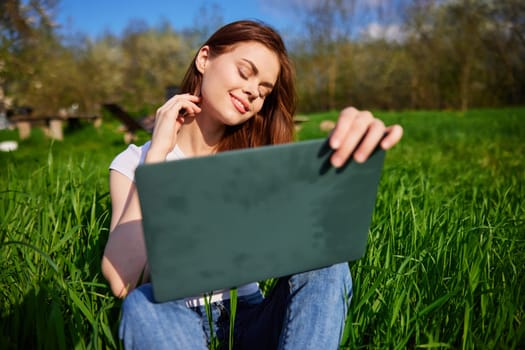 woman working freelance with laptop sitting in high grass field. High quality photo