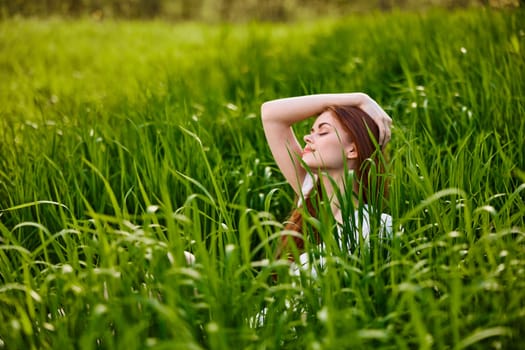 cute woman with red hair sits in tall green grass with her hand on her head. High quality photo