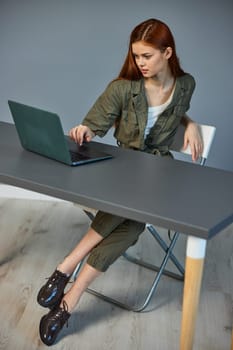 photo of a woman sitting at a table with a laptop in the office against the background of a blue wall. High quality photo